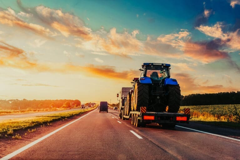 heavy industrial truck semi trailer flatbed platform transport two big modern farming tractor machine on common highway road at sunset sunrise sky